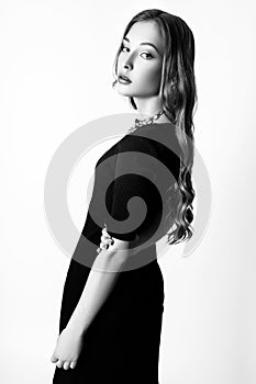 Fashion portrait of beautiful young woman with blond hair. Girl in a black dress and blue necklace on a white background. Black an