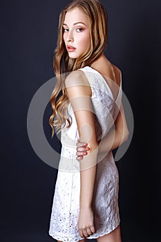 Fashion portrait of beautiful young woman with blond hair. Girl in a white summer dress on a black background