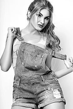 Fashion portrait of beautiful young woman with long hair. Girl in a white jersey and denim overalls on a white background. Black a