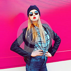 Fashion portrait blonde cool girl sending sweet air kiss posing in rock black style jacket, hat posing on city street