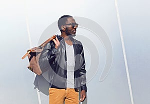 Fashion portrait elegant african man wearing a sunglasses and black rock leather jacket with bag in the city, copy space empty