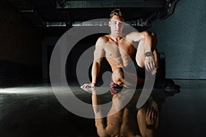 Fashion portrait of a fitness model of a bodybuilder man sitting on the mirror floor after a workout.