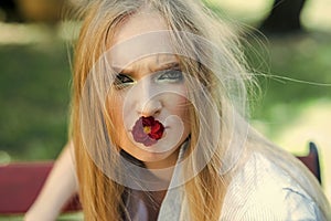 Fashion portrait. Girl with blonde hair and makeup hold red flower in mouth from blossoming tree in spring outdoor