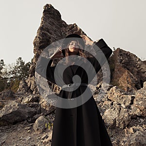 Fashion portrait of a girl dressed in coat and hat. Rocks at background