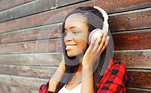 Fashion portrait happy smiling african woman with headphones is enjoying listens to music over background