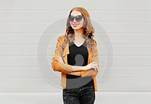 Fashion portrait happy smiling woman with crossed arms wearing a sunglasses, jacket over grey
