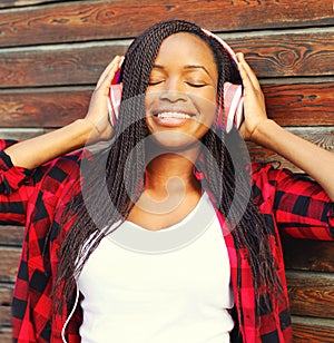 Fashion portrait happy smiling young african woman with headphones enjoying listens to music