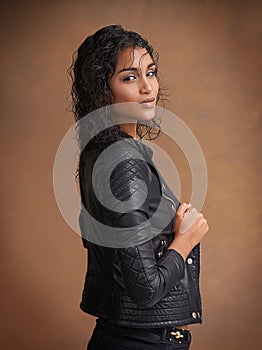 Fashion, portrait and leather jacket with woman, confident and stylish clothes on brown studio background. Face, Indian