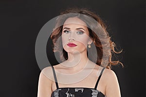 Fashion portrait of nice young brunette woman with makeup and long windy wavy hair looking at camera on black background