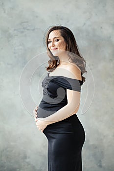 Fashion portrait of pregnant woman in black dress on gray