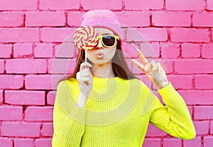 Fashion portrait pretty cool girl with lollipop having fun over pink background