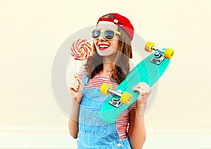 Fashion portrait pretty cool smiling girl with a lollipop and skateboard over white