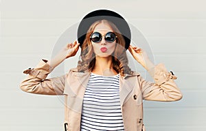 Fashion portrait pretty sweet young woman blowing red lips wearing a black hat sunglasses coat over grey