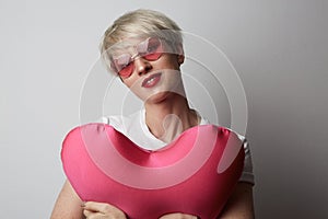 Fashion portrait pretty sweet young woman with red lips hugging a plush heart wearing white tshort over white background