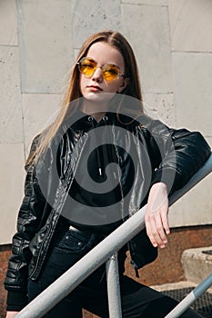 Fashion portrait pretty teenager girl in sunglasses and black rock style over city background