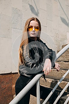 Fashion portrait pretty teenager girl in sunglasses and black rock style over city background