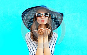 Fashion portrait pretty woman with red lips is sends an air kiss in straw summer hat over colorful blue