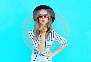 Fashion portrait pretty woman with red lips is sends an air kiss in a sunglasses shape of heart over blue