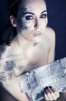 Fashion portrait of pretty young woman with creative make up like a snake, fashion victim with python skin clutch luxury