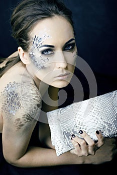 Fashion portrait of pretty young woman with creative make up like a snake, fashion victim with python skin clutch luxury