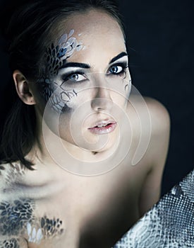 Fashion portrait of pretty young woman with creative make up like a snake, fashion victim with python skin clutch luxury