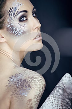 Fashion portrait of pretty young woman with creative make up like a snake, fashion victim with python skin clutch luxury