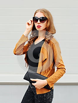 Fashion portrait pretty young woman wearing sunglasses jacket and black handbag clutch over grey