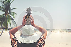 Fashion portrait rear of beautiful woman with fresh pineapple holds up - vacation on tropical beach in summer