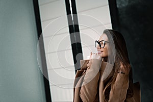 Fashion portrait of a stylish girl in glasses and ligth brown coat. Selective focus from side on model girl. Closeup.