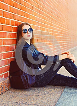 Fashion portrait woman in black rock style sitting over bricks background