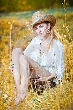 Fashion portrait woman with hat and white shirt sitting on a hay stack