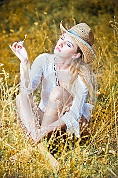 Fashion portrait woman with hat and white shirt sitting on a hay stack