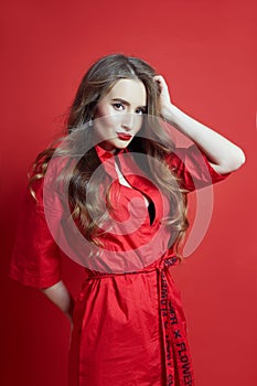 Fashion portrait of woman in red dress, beautiful makeup, curly long hair. Girl perfect lip makeup on red background