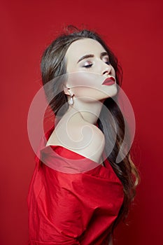 Fashion portrait of woman in red dress, beautiful makeup, curly long hair. Girl perfect lip makeup on red background