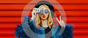 Fashion portrait of woman with retro camera taking picture blowing red lips sending sweet air kiss wearing blue faux fur coat