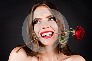 Fashion portrait of young beautiful woman with red rose on black background. Rose flowers in a mouth. Sensual woman
