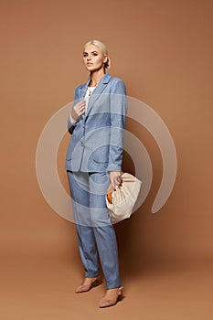 A fashion portrait of a young business lady in an elegant blue suit posing with stylish purse on the beige background