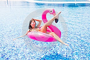 Fashion portrait of a young and girl in the pool on an inflatable pink flamingo in a bathing suit and sunglasses in summer. P