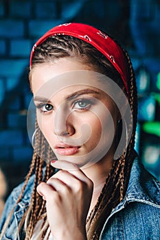 Fashion portrait of young hipster woman with bandana and braids on color wall