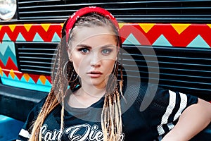 Fashion portrait of young hipster woman with bandana and long braids sitting on city street