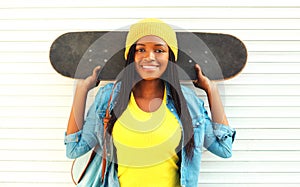 Fashion portrait young smiling african woman with skateboard in colorful clothes over white