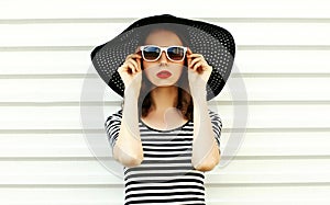 Fashion portrait young woman in black summer straw hat posing on white wall