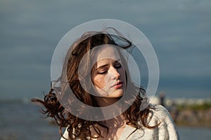 Fashion portrait of young woman model with brown hair and natural make-up walking along the shore of the resort on a spring