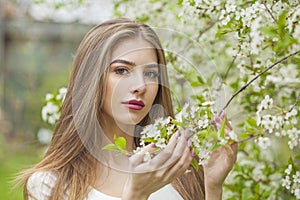 Fashion portrait of young woman with natural makeup and healthy long brown hair in blossom park outdoors. Natural female beauty