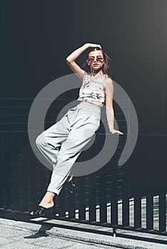 Fashion portrait of young woman wearing sunglasses, top, slingbacks, blue suit. Young beautiful happy model posing near photo