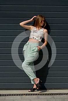 Fashion portrait of young woman wearing sunglasses, top, slingbacks, blue suit. Young beautiful happy model posing near photo