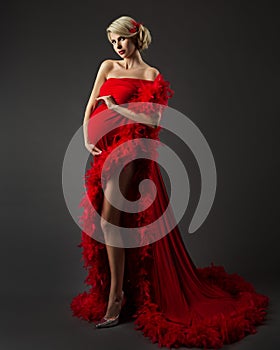 Fashion Pregnant Woman in Luxury Red Dress over Black. Elegant Mother embracing Belly in evening Gown with Feather. Pregnancy