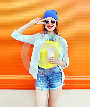 Fashion pretty cool girl with coffee cup listens to music over colorful orange