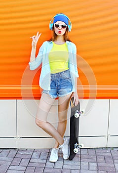 Fashion pretty cool girl with skateboard listens to music over colorful orange