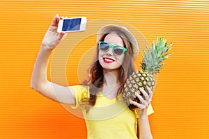 Fashion pretty cool girl in sunglasses, hat with pineapple taking picture selfie on smartphone over colorful